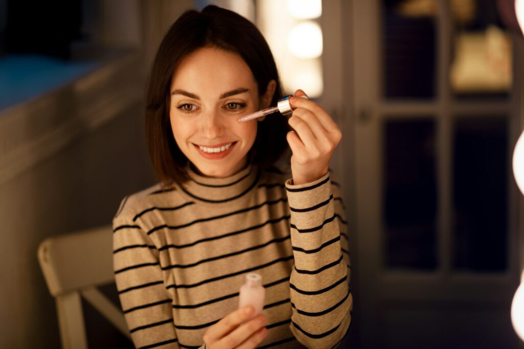 Cheerful young woman applying hydrating serum on her face