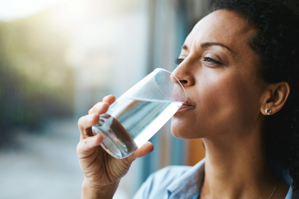 Keep calm and hydrate on. Shot of a woman drinking a glass of water at home.