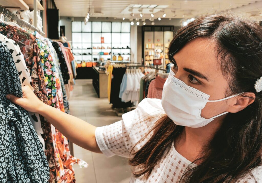 Young woman with protective face mask looking at clothes in retail store.