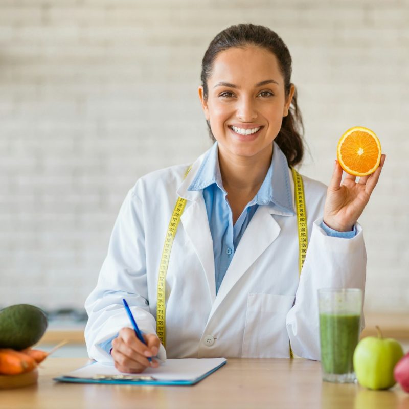 Dietician with orange in kitchen, writing nutrition plan