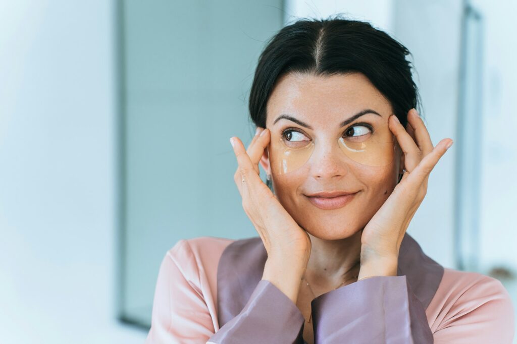 Young adult brunette caucasian woman with skin care patches applied on face touches skin. Morning